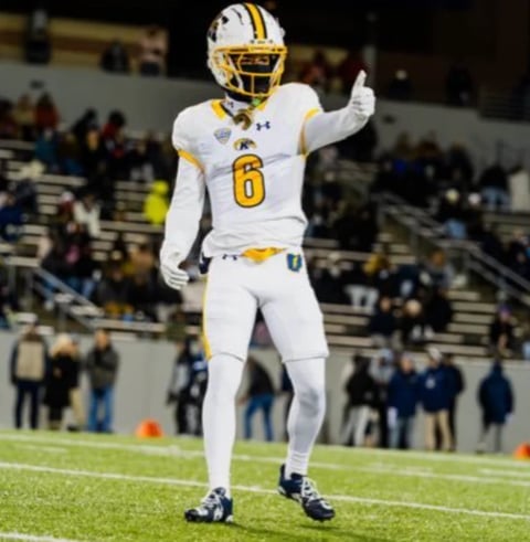 Football player wearing white and gold uniform with number 6 gesturing on the field during a night game with stadium crowd in background