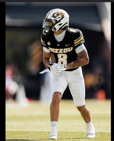 Football player wearing Mizzou black and gold uniform number 8 with white helmet in ready stance on field